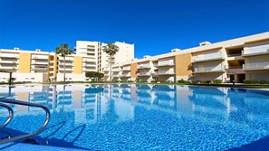 Una piscina con acqua cristallina e azzurra, circondata da edifici a più piani con balconi.