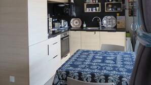 A compact kitchen with a microwave, oven, and sink. There are shelves with decorative items and a table with a patterned tablecloth. - 5-seater cottage in Pomérols (Pomérols)