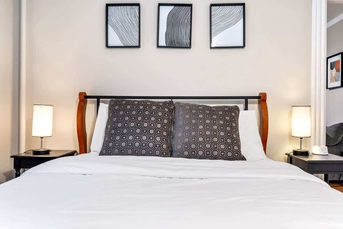 A neatly made bed with patterned pillows, two bedside lamps, and three framed artworks on the wall.