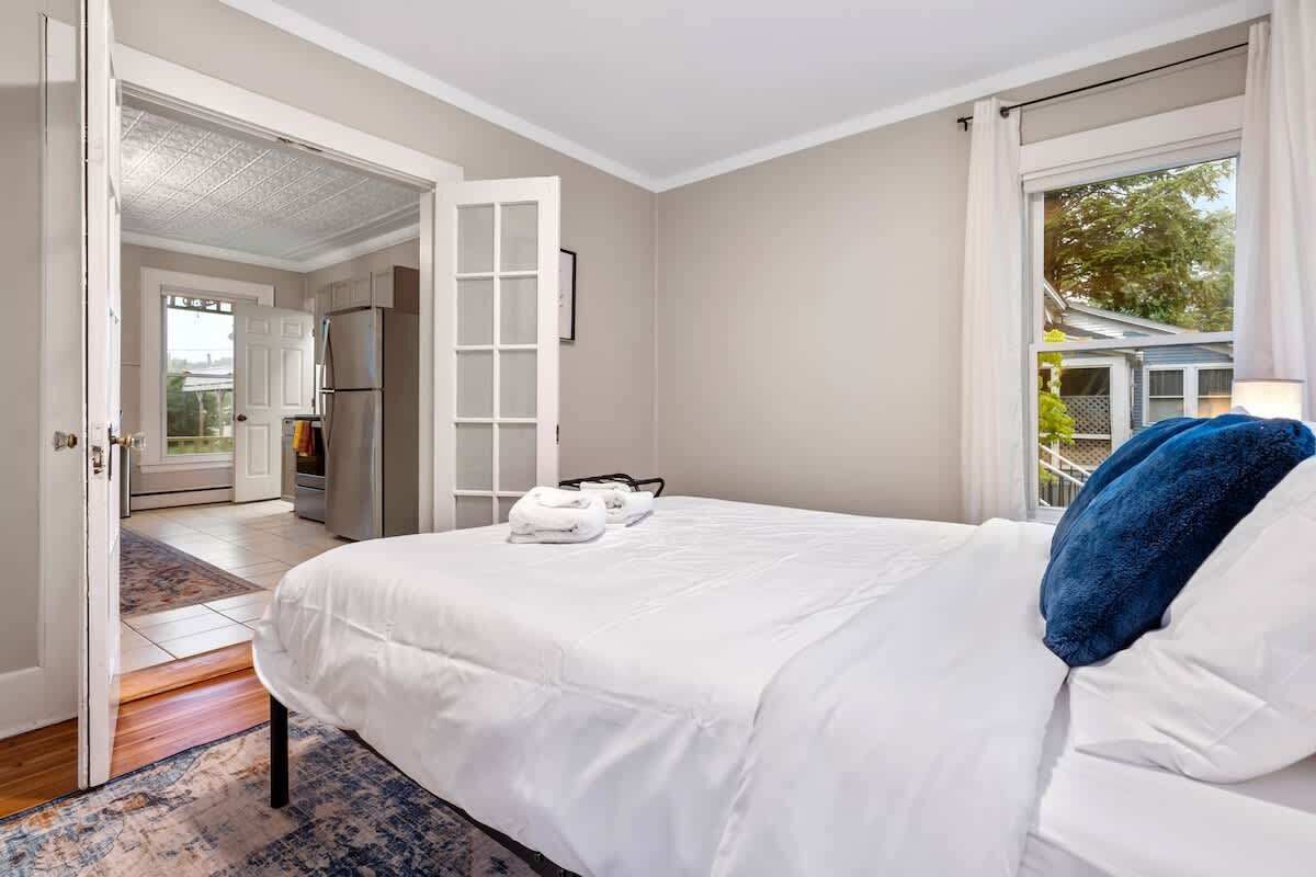 Un dormitorio con una cama grande, una puerta blanca que da a un balcón y vistas al exterior.