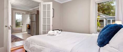 Un dormitorio con una cama grande, una puerta blanca que da a un balcón y vistas al exterior.