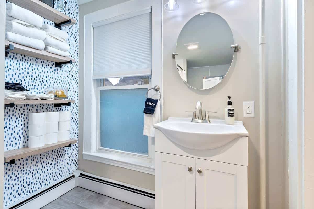 A bathroom with a white sink, a round mirror, and shelves with towels and toiletries.