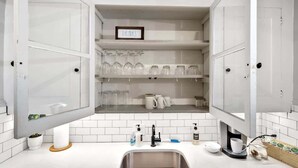 Una cocina con armarios blancos, un lavamanos y un cartel que dice 'Bebidas' sobre las repisas.
