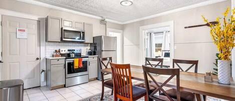 A modern kitchen with stainless steel appliances, a dining area with wooden chairs, and a patterned rug on the floor.