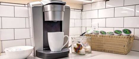 Een keuken met een koffiezetapparaat, een witte mok, een kom en een mandje theezakjes.