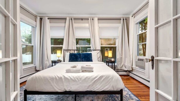 Un dormitorio con una cama grande, cortinas blancas y vistas a través de las ventanas.