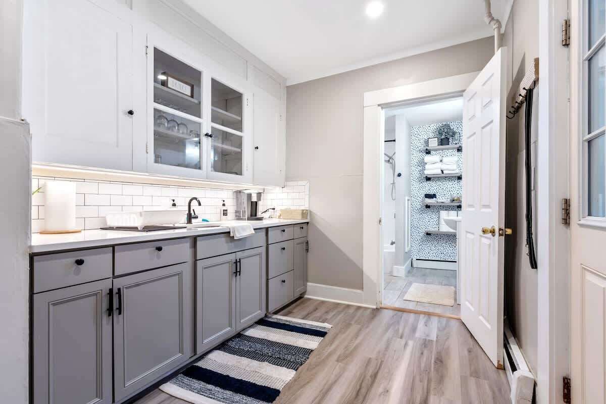 A modern kitchen with grey cabinets, white countertops, and a striped rug.