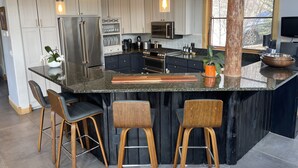 A modern kitchen with a large island, bar stools, and a wooden accent column. - Comfortable large mountain home with stunning views, hot tub and pool table! (Telluride)