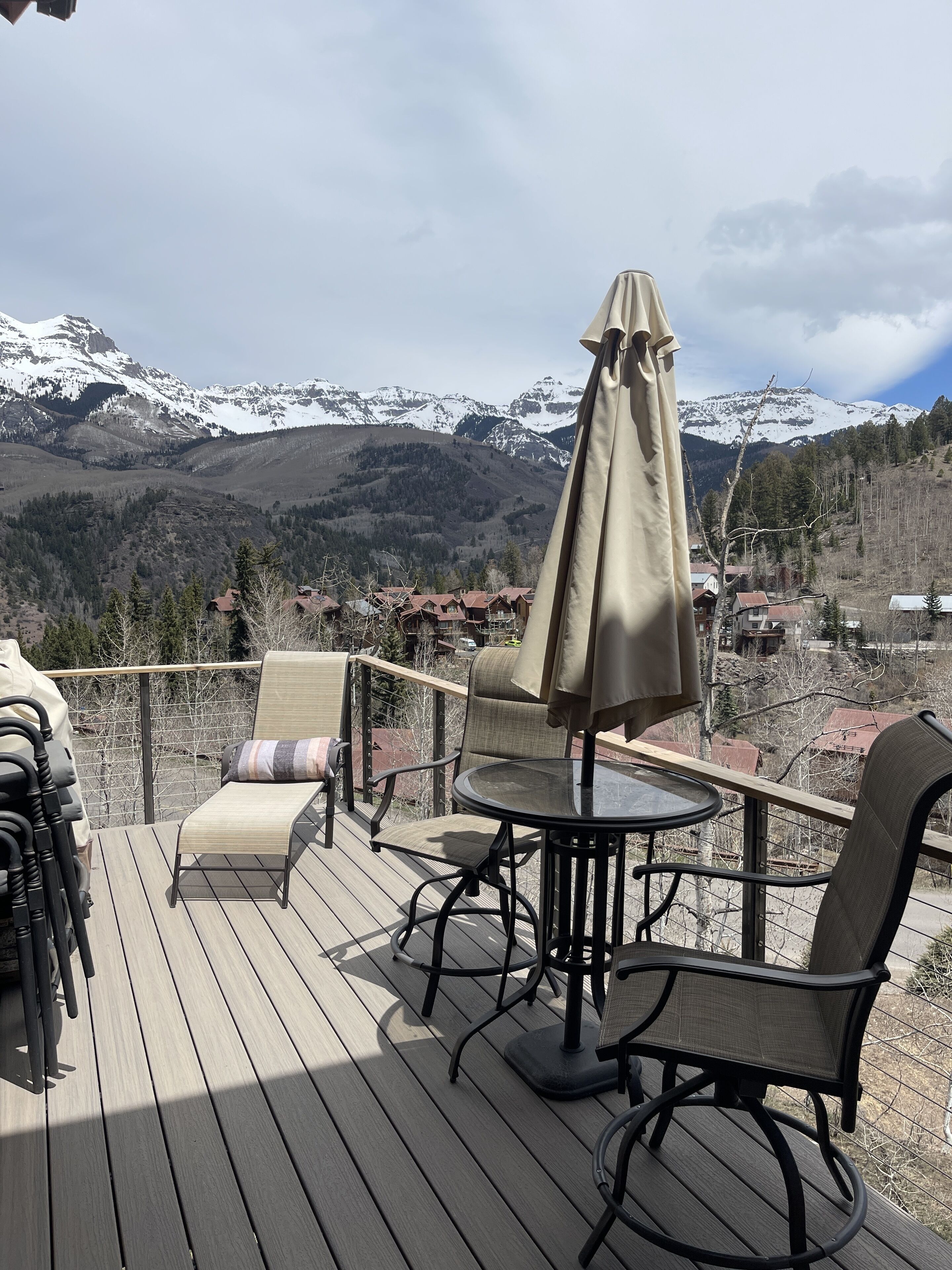 A deck with outdoor furniture, including chairs and a table, overlooking a mountainous landscape with snow-capped peaks.
