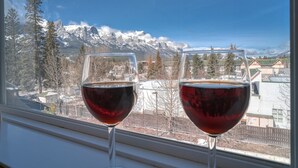 Dos copas de vino en un alféizar con vista a montañas nevadas y un pueblo al fondo.