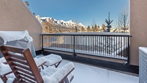 Un balcón con vistas a montañas nevadas, una silla de madera y una barandilla de metal.