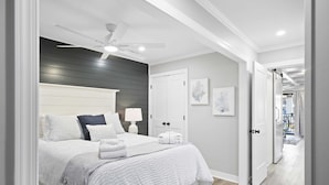 Une chambre à coucher avec un lit, des lampes de chevet, un ventilateur de plafond et une porte donnant sur une autre pièce.