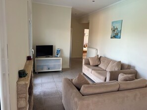 A living room with a beige sofa, a television on a stand, and a painting on the wall.