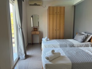A hotel room with two beds, a wooden wardrobe, a small bedside table with a mirror, and a window with curtains.