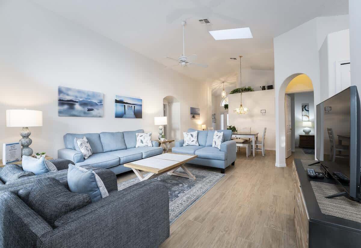 Een moderne woonkamer met een zithoek, een salontafel en een televisie. Er is een eethoek met een tafel en stoelen, en een keuken met een koelkast.