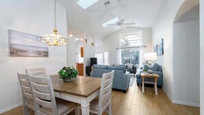 A spacious living area with a dining table, chairs, a sofa, and a ceiling fan.
