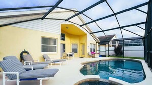 A covered outdoor swimming pool area with lounge chairs and a hot tub.