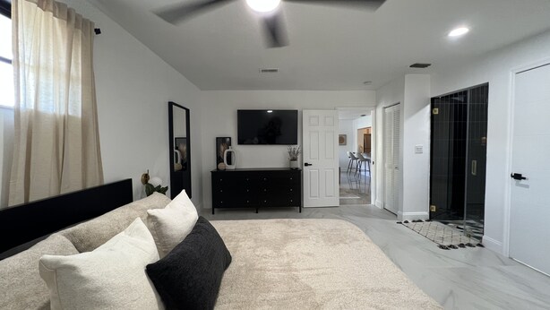 A bedroom with a bed, a ceiling fan, a TV, a dresser, and a door leading to a bathroom.