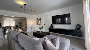En moderne stue med en grå sofa, et sofabord og et fladskærms-TV monteret på væggen.
