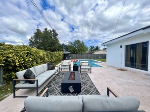 A modern outdoor patio with a pool, a sofa set, and a dining area.