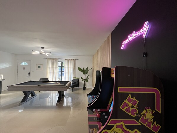 A modern room with a pool table, a neon sign, and a retro arcade machine.