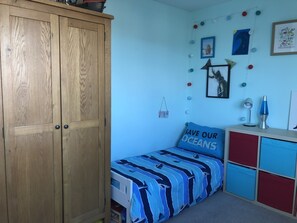 A bedroom with a bed, a wardrobe, a desk with a lamp, and wall decorations.