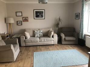 A living room with a beige sofa, a patterned throw pillow, a side table with a lamp, and a blue rug.