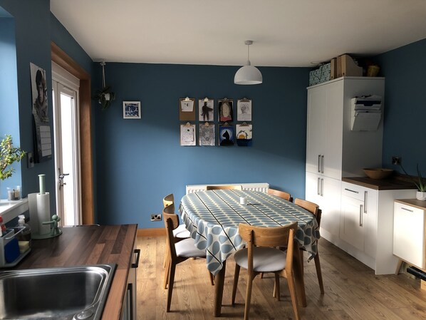 A kitchen with a dining table, wooden chairs, a hanging light fixture, and a white refrigerator.