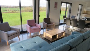 Ein modernes Wohnzimmer mit einem großen blauen Sofa, zwei Sesseln, einem Couchtisch und einem Essbereich mit Stühlen und Tisch.