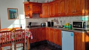 A kitchen with wooden cabinets, a microwave, a coffee maker, and a dining area with a table and chairs. - Apartments Finca House Garden (Tijarafe. La Palma)