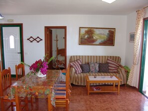 A living room with a dining table, chairs, a sofa, and a painting on the wall.