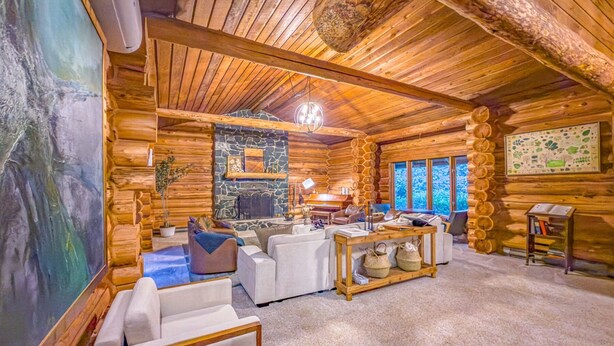 A log cabin interior with a stone fireplace, white furniture, and a large painting.