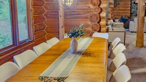 A wooden dining table with white chairs, a vase with greenery, and a hanging light fixture.