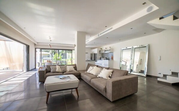 A modern living room with a sectional sofa, a coffee table, and a kitchen area visible through an open door.