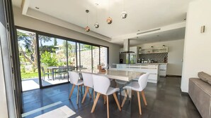 A modern kitchen with a central island, a dining area with white chairs, and a large sliding glass door leading to an outdoor patio. - ★★La Magnifique★★Piscine/Spacieux/Paisible (LE CANNET)