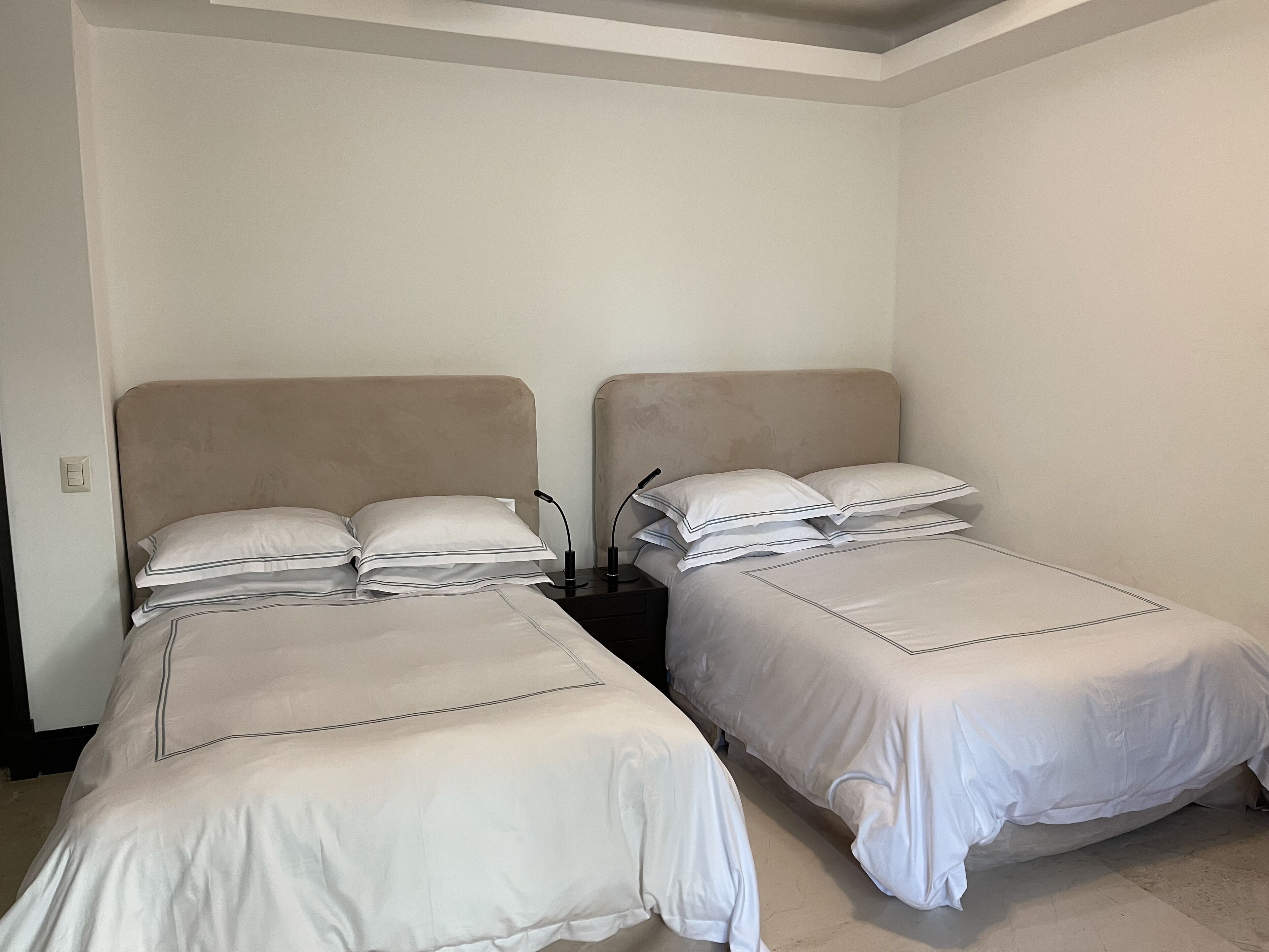 Dos camas individuales con cabeceras, ropa de cama blanca y mesitas de noche con lámparas.