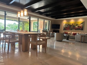 Relax in a spacious living area with a dining table, flat-screen TV, and a large window offering a view of the surrounding greenery.