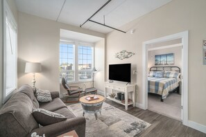 A living room with a sofa, a coffee table, a TV, and a bed in the adjacent room.