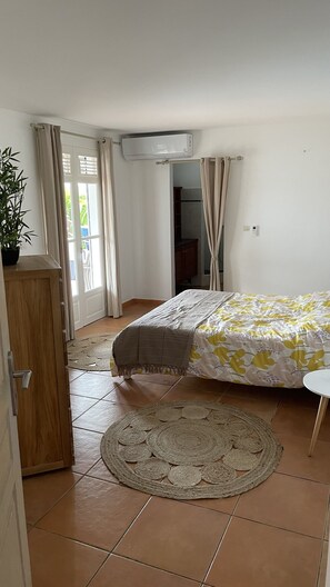 A bedroom with a bed, a bedside table, a potted plant, a door, and an air conditioning unit.