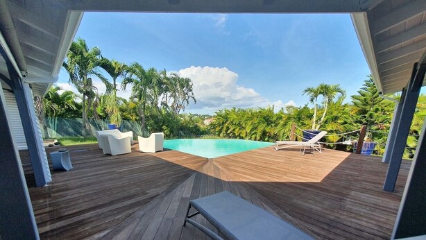 A wooden deck with a pool, lounge chairs, and white sofas. - Villa (Baie-Mahault)