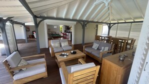 A spacious covered outdoor area with wooden furniture, including sofas and a coffee table, and a dining area with wooden tables and chairs. - Villa (Baie-Mahault)