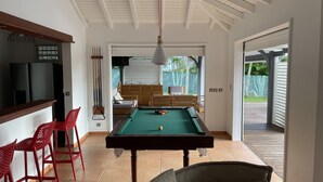 A pool table in a room with a wooden ceiling, a television, and red chairs. - Villa (Baie-Mahault)