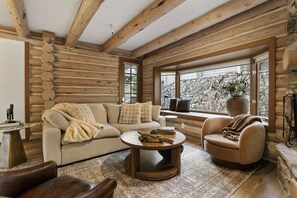 A log cabin interior with a sofa, armchair, coffee table, and a stone wall outside.