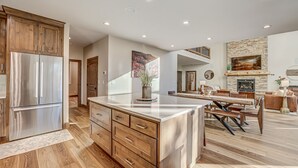 Une cuisine moderne avec des meubles en bois, un réfrigérateur en acier inoxydable et un coin repas comprenant une table et des bancs en bois.
