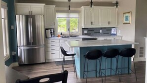 A modern kitchen with white cabinets, stainless steel appliances, a large island with bar stools, and pendant lighting.
