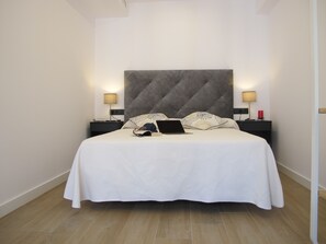 Una cama bien hecha con un ordenador portátil, dos lámparas de noche y una mesita de noche con una vela roja.