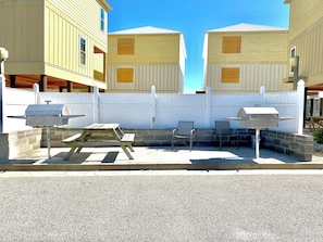 Eine Terrasse mit Grill, einem Holztisch und zwei Stühlen.