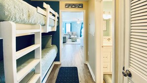 Un pasillo con literas, una puerta con espejo y un letrero que dice 'Peace, Love & Sandy Feet'.
