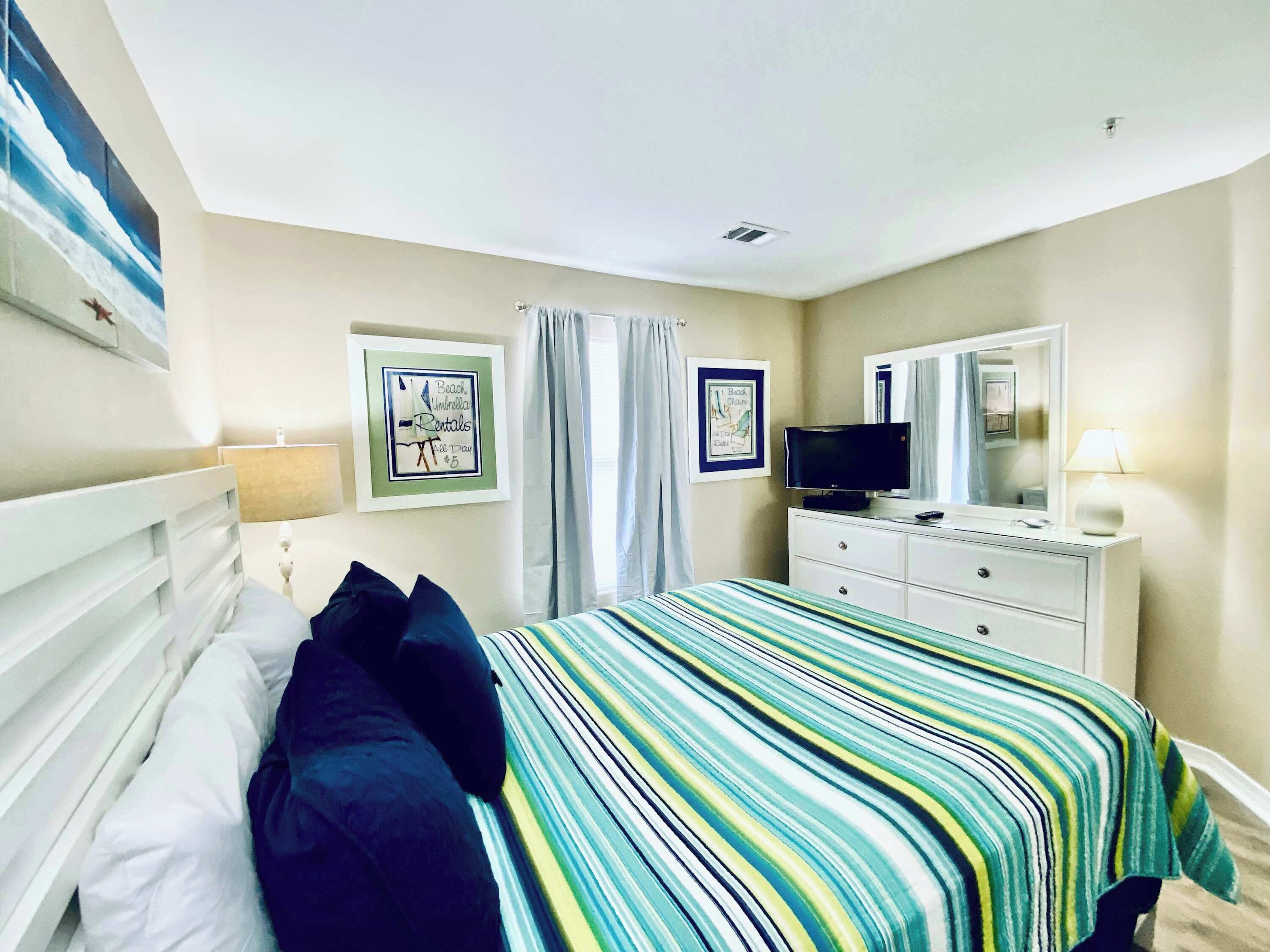 A bedroom with a bed, a television, a dresser, and two framed pictures on the wall.