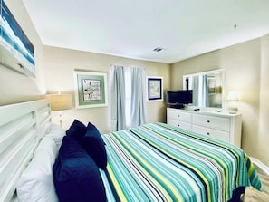 Une chambre à coucher comprenant un lit, une télévision, une commode et deux tableaux encadrés accrochés au mur.
